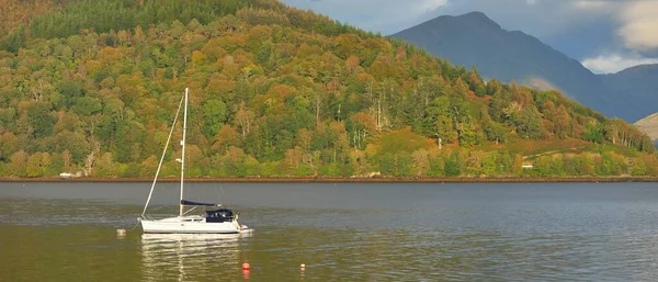 Sailboat anchored in lake. Majestic forest hills. Scotland, UK. Atmospheric landscape. Travel destinations, sailing, cruising, eco tourism, hiking, nature, environmental conservation