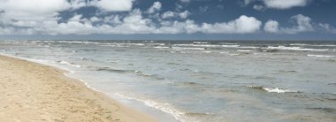 Güneşli bir günde Baltık Denizi kıyısı. Kumsal, kum tepeleri. Fırtınadan sonra dramatik gökyüzü, parlayan bulutlar.. Doğa, tatiller, eğlence. eko turizm