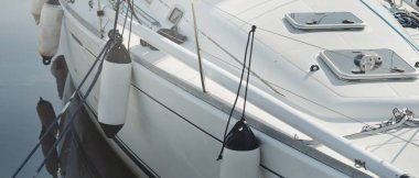 White modern sailboat (for rent and sale) moored to a pier in a yacht marina. Wooden teak deck. Nautical vessel, transportation, amateur sailing, vacations, cruising, recreation concepts