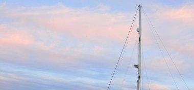 Yelkenli bir yatın direğinin alçak açılı görüntüsü. Yumuşak güneş ışığı, parlayan günbatımı gökyüzü. Ulaşım, eğlence, eğlence, gezi, spor, yelkencilik, yarış, yat