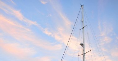 Yelkenli bir yatın direğinin alçak açılı görüntüsü. Yumuşak güneş ışığı, parlayan günbatımı gökyüzü. Ulaşım, eğlence, eğlence, gezi, spor, yelkencilik, yarış, yat