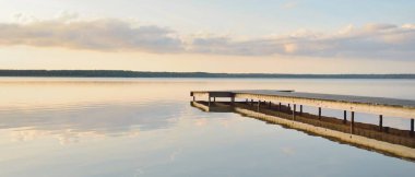 Forest lake (river) at sunset. Wooden pier. Glowing clouds, symmetry reflections in a still crystal clear water. Idyllic landscape. Nature, ecology, ecological reserve, ecotourism, hiking, vacations