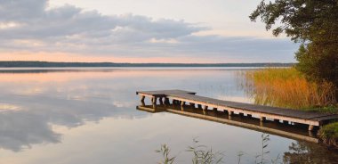 Orman Gölü (nehir) gün batımında. Ahşap iskele. Parlayan bulutlar, durgun ve berrak suda simetri yansımaları. Idyllic manzara. Doğa, ekoloji, ekolojik rezerv, eko-turizm, yürüyüş, tatiller