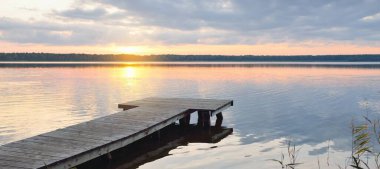 Orman Gölü (nehir) gün batımında. Ahşap iskele. Parlayan bulutlar, durgun ve berrak suda simetri yansımaları. Idyllic manzara. Doğa, ekoloji, ekolojik rezerv, eko-turizm, yürüyüş, tatiller