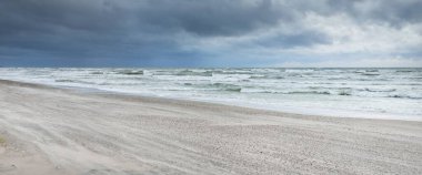 Baltık kıyıları (kum tepeleri) fırtınadan sonra gün batımında. Dramatik gökyüzü, parlayan bulutlar, rüzgar. Sonbahar manzarası. Doğa, çevre, ekoloji, kararsız hava, iklim değişikliği