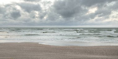 Baltık kıyıları (kum tepeleri) fırtınadan sonra gün batımında. Dramatik gökyüzü, parlayan bulutlar, rüzgar. Sonbahar manzarası. Doğa, çevre, ekoloji, kararsız hava, iklim değişikliği