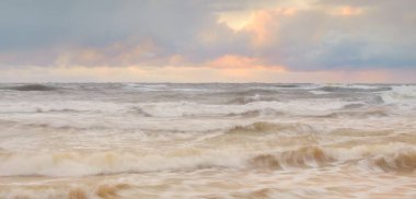 Baltic sea at sunset. Dramatic sky, blue and pink glowing clouds, golden sunlight. Waves, splashing water. Picturesque scenery, seascape, nature. Panoramic view, long exposure