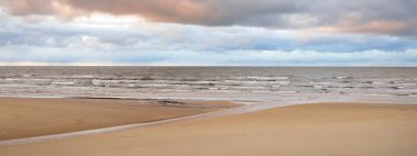 Gün batımında Baltık kıyısı. Kumsal manzarası (kum tepeleri). Dramatik günbatımı gökyüzü, parlayan bulutlar. Idyllic manzara. Doğa, tatiller, eğlence. Çevre turizmi. Panoramik görünüm