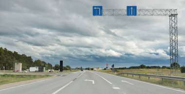 Tarlalar ve orman boyunca (asfalt yol) yol. Arabadan bak. Dramatik fırtına bulutları. Seyahat yerleri, rotalar, tatiller, lojistik, uzak yerler