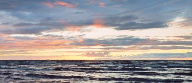 Gün batımında Baltık kıyılarından panoramik manzara. Dramatik fırtına gökyüzü, parlayan bulutlar, altın güneş ışığı. Dalgalar, su sıçratma. Doğa, çevre, kararsız hava