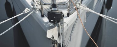 Beyaz modern yelkenli (kiralık ve satılık) yat limanındaki bir rıhtıma demirlemiş. Tahta meşe güvertesi. Denizcilik, ulaşım, amatör yelkencilik, tatiller, gezinti, eğlence kavramları