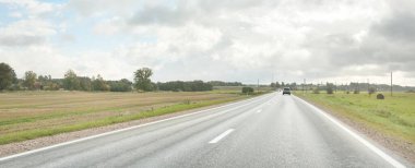 Tarlalar ve orman boyunca (asfalt yol) yol. Arabadan bak. Dramatik fırtına bulutları. Seyahat yerleri, rotalar, tatiller, lojistik, uzak yerler