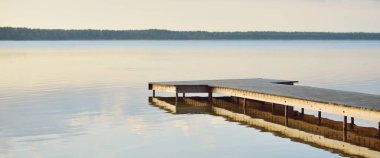 Orman Gölü (nehir) gün batımında. Ahşap iskele. Parlayan bulutlar, durgun ve berrak suda simetri yansımaları. Idyllic manzara. Doğa, ekoloji, ekolojik rezerv, eko-turizm, yürüyüş, tatiller
