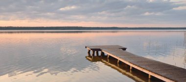 Orman Gölü (nehir) gün batımında. Ahşap iskele. Parlayan bulutlar, durgun ve berrak suda simetri yansımaları. Idyllic manzara. Doğa, ekoloji, ekolojik rezerv, eko-turizm, yürüyüş, tatiller