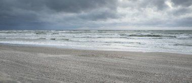 Baltık kıyıları (kum tepeleri) fırtınadan sonra gün batımında. Dramatik gökyüzü, parlayan bulutlar, rüzgar. Sonbahar manzarası. Doğa, çevre, ekoloji, kararsız hava, iklim değişikliği