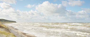 Fırtınadan sonra Baltık kıyıları (kum tepeleri, plaj). Dramatik gökyüzü, parlayan bulutlar. Resimli panoramik manzara. Doğa, çevre, ekoloji, eko-turizm, yürüyüş, keşif kavramları