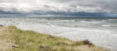 Fırtınadan sonra Baltık kıyısı (plaj). Kum tepeleri, kum tepeleri. Dramatik gökyüzü, dalgalar ve su sıçramaları. Doğa, ekoloji, kararsız hava, iklim değişikliği, eko-turizm, yürüyüş kavramları