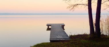 Forest lake (river) at sunrise. Wooden pier (boardwalk), mighty trees. Soft sunlight, mist, reflections on water. Idyllic autumn landscape. Pure nature, ecotourism, hiking, exploring