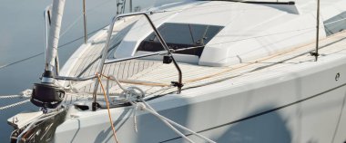 Beyaz modern yelkenli (kiralık ve satılık) yat limanındaki bir rıhtıma demirlemiş. Tahta meşe güvertesi. Denizcilik, ulaşım, amatör yelkencilik, tatiller, gezinti, eğlence kavramları