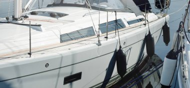 White modern sailboat (for rent and sale) moored to a pier in a yacht marina. Wooden teak deck. Nautical vessel, transportation, amateur sailing, vacations, cruising, recreation concepts