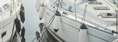 White modern sailboat (for rent and sale) moored to a pier in a yacht marina. Nautical vessel, transportation, amateur sailing, sport, leisure activity, vacations, cruising, recreation concepts
