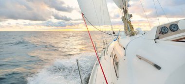 Gün batımında açık denizde yelken açmak. Güvertenin yakın görüntüsü, direk ve yelkenler. Yağmurdan sonra açık gökyüzü, çarpıcı parlayan bulutlar, altın güneş ışığı, dalgalar ve su sıçramaları, kasırga. Destansı deniz manzarası