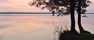 Gün batımında Orman Gölü. Güçlü ağaçlar. Yumuşak güneş ışığı, parlayan bulutlar kristal berrak suda simetri yansımaları. Idyllic manzara. Panoramik manzara. Doğa, ekoloji, çevrecilik. Barış ve neşe kavramı