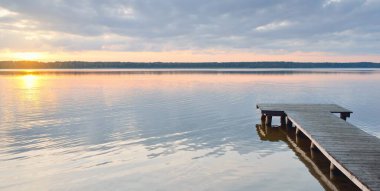 Orman Gölü (nehir) gün batımında. Ahşap iskele. Parlayan bulutlar, durgun ve berrak suda simetri yansımaları. Idyllic manzara. Doğa, ekoloji, ekolojik rezerv, eko-turizm, yürüyüş, tatiller