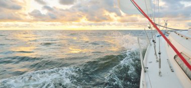 Gün batımında açık denizde yelken açmak. Güvertenin yakın görüntüsü, direk ve yelkenler. Yağmurdan sonra açık gökyüzü, çarpıcı parlayan bulutlar, altın güneş ışığı, dalgalar ve su sıçramaları, kasırga. Destansı deniz manzarası