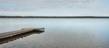Orman nehri (göl) güneşli bir günde. Ahşap iskele. Clea gökyüzü, kristal berrak suda yansıyor. Idyllic manzara, kırsal manzara. Doğa, ekoloji, eko-turizm, yürüyüş, ekoloji beldesi, yerel turizm