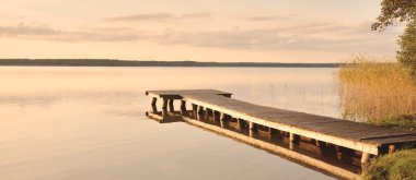 Orman Gölü (nehir) gün batımında. Ahşap iskele. Parlayan bulutlar, durgun ve berrak suda simetri yansımaları. Idyllic manzara. Doğa, ekoloji, ekolojik rezerv, eko-turizm, yürüyüş, tatiller