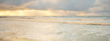 Gün batımında Baltık Denizi. Dramatik gökyüzü, mavi ve pembe parlayan bulutlar, altın güneş ışığı. Dalgalar, su sıçratma. Resimli manzara, deniz manzarası, doğa. Panoramik görünüm, uzun pozlama