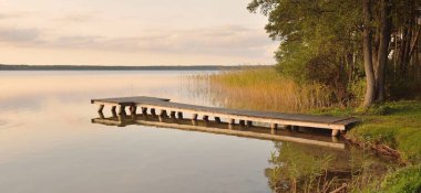 Orman Gölü (nehir) gün batımında. Ahşap iskele. Parlayan bulutlar, durgun ve berrak suda simetri yansımaları. Idyllic manzara. Doğa, ekoloji, ekolojik rezerv, eko-turizm, yürüyüş, tatiller