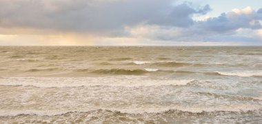 Gün batımında Baltık Denizi. Dramatik gökyüzü, mavi ve pembe parlayan bulutlar, altın güneş ışığı. Dalgalar, su sıçratma. Resimli manzara, deniz manzarası, doğa. Panoramik görünüm, uzun pozlama