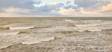 Gün batımında Baltık Denizi. Dramatik gökyüzü, mavi ve pembe parlayan bulutlar, altın güneş ışığı. Dalgalar, su sıçratma. Resimli manzara, deniz manzarası, doğa. Panoramik görünüm, uzun pozlama