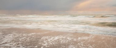 Gün batımında Baltık Denizi. Dramatik gökyüzü, mavi ve pembe parlayan bulutlar, altın güneş ışığı. Dalgalar, su sıçratma. Resimli manzara, deniz manzarası, doğa. Panoramik görünüm, uzun pozlama