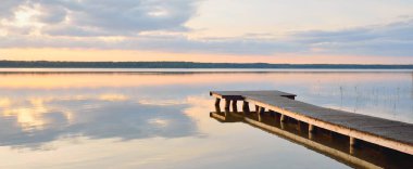 Forest lake (river) at sunset. Wooden pier. Glowing clouds, symmetry reflections in a still crystal clear water. Idyllic landscape. Nature, ecology, ecological reserve, ecotourism, hiking, vacations