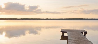 Forest lake (river) at sunset. Wooden pier. Glowing clouds, symmetry reflections in a still crystal clear water. Idyllic landscape. Nature, ecology, ecological reserve, ecotourism, hiking, vacations