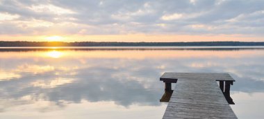 Orman Gölü (nehir) gün batımında. Ahşap iskele. Parlayan bulutlar, durgun ve berrak suda simetri yansımaları. Idyllic manzara. Doğa, ekoloji, ekolojik rezerv, eko-turizm, yürüyüş, tatiller