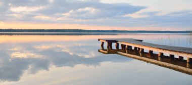 Orman Gölü (nehir) gün batımında. Ahşap iskele. Parlayan bulutlar, durgun ve berrak suda simetri yansımaları. Idyllic manzara. Doğa, ekoloji, ekolojik rezerv, eko-turizm, yürüyüş, tatiller