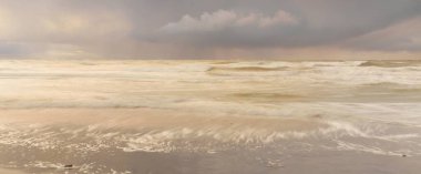 Gün batımında Baltık Denizi. Dramatik gökyüzü, mavi ve pembe parlayan bulutlar, altın güneş ışığı. Dalgalar, su sıçratma. Resimli manzara, deniz manzarası, doğa. Panoramik görünüm, uzun pozlama