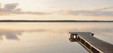 Forest lake (river) at sunset. Wooden pier. Glowing clouds, symmetry reflections in a still crystal clear water. Idyllic landscape. Nature, ecology, ecological reserve, ecotourism, hiking, vacations