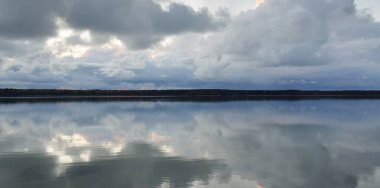 Gün batımında Orman Nehri (Lake). Dramatik gökyüzü, karanlık, parlak bulutlar. Kristal berrak suda simetri yansımaları. Panoramik sonbahar manzarası. Doğa, çevre, ekoloji, hava durumu, iklim değişikliği