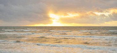 Gün batımında Baltık kıyılarından panoramik manzara. Dramatik bulutlar, parlayan bulutlar, fırtınadan sonra altın güneş ışığı. Doğa, çevre, iklim değişikliği, kararsız hava