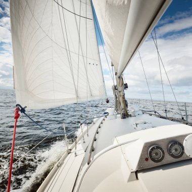 Açık bir günde açık denizde yelken açan beyaz yelkenli bir yat. Güverteden pruvaya bir manzara. Kümülüs bulutları. Ulaşım, seyahat, gezi, spor, eğlence, boş zaman aktivitesi, yarış, yelkenli yarışı