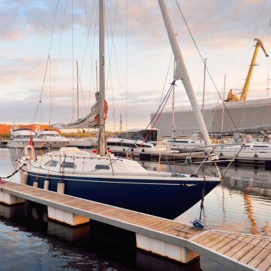 Günbatımında yat limanında demirlemiş zarif ve modern yelkenliler. Dramatik gökyüzü, parlayan altın bulutlar. Tatiller, ulaşım, spor, eğlence, turizm, seyahat, liman