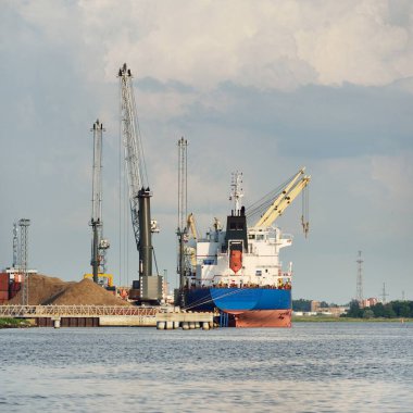 Büyük kargo gemisi (toplu taşıyıcı, 187 metre uzunluğunda) iskele terminalinde yükleme, arka planda vinçler. Yük taşımacılığı, lojistik, küresel iletişim, ekonomi, ticaret, sanayi