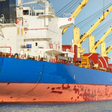 Büyük kargo gemisi (toplu taşıyıcı, 187 metre uzunluğunda) iskele terminalinde yükleme, arka planda vinçler. Yük taşımacılığı, lojistik, küresel iletişim, ekonomi, ticaret, sanayi