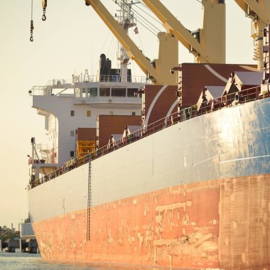 Liman terminalinde büyük bir kargo gemisi yükleniyor, arka planda vinçler var. Yük taşımacılığı, deniz taşımacılığı, lojistik, küresel iletişim, dünya çapında taşımacılık, ekonomi, ticaret, sanayi