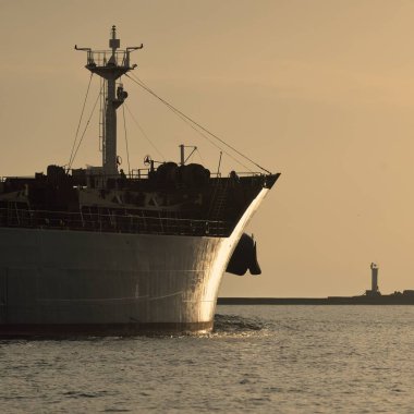 Vinçleri olan büyük bir kargo gemisi gün batımında limandan ayrılıyor. Baltık Denizi. Dramatik fırtına gökyüzü. Yük taşımacılığı, lojistik, küresel iletişim, ekonomi, ticaret, sanayi